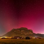 a field with a mountain in the background and stars in the sky